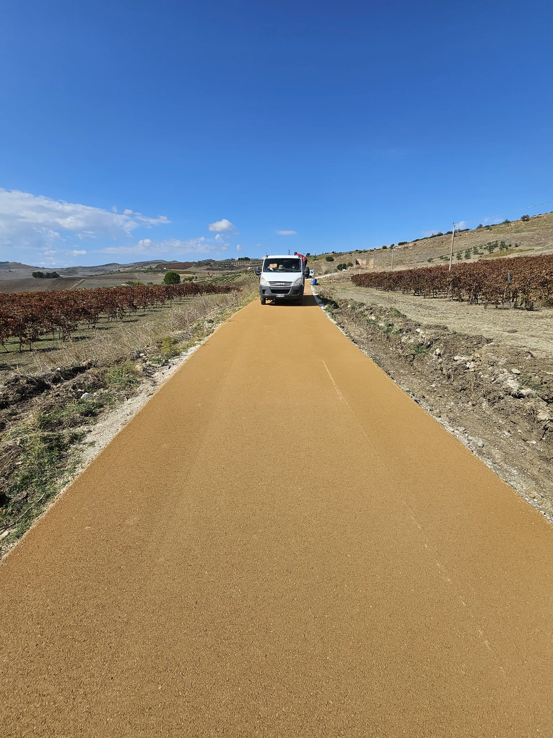 Camino agrícola con pavimento terrizo estabilizado entre viñedos · Sicilia